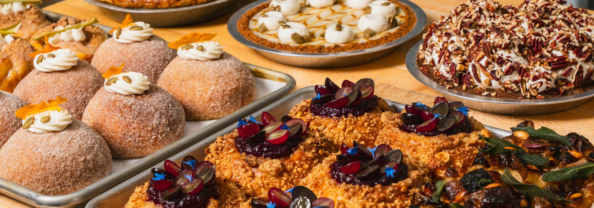 A Sunday spread on the Manifold counter: sugared pepita-cream babka buns, pumpkin and pecan cream pies, peanut-and-grape brioche squares, and squash-and-sage focaccia